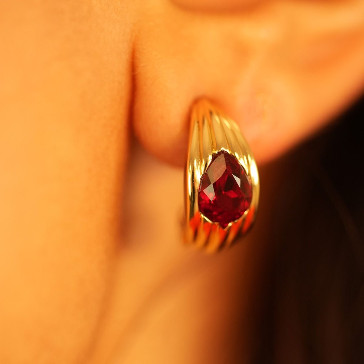 The Praline Huggie Earring ingeniously imitates the praline's texture through debossed vertical scoring. Its cocooned huggie design encases a teardrop stone at the centre, adding a burst of vivid colour. 