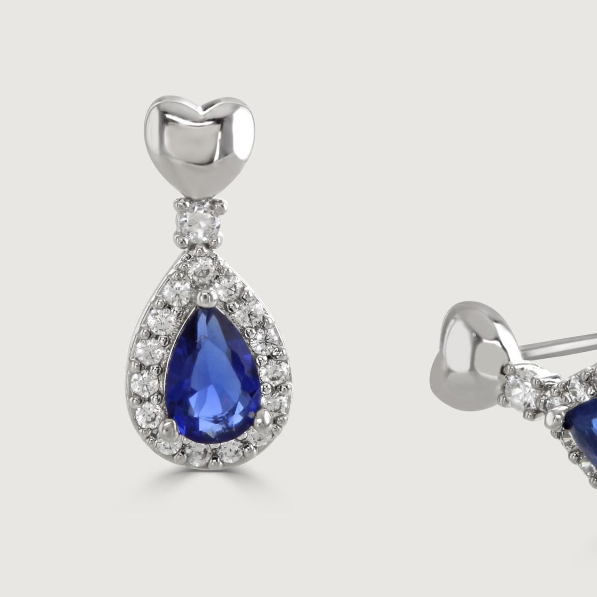 Discover elegance with our Sapphire Heart Pear-Drop Earrings. Enhanced by cubic zirconia pear-drop band, it features a polished heart at the stud. The enchanting focal point is a captivating sapphire stone.