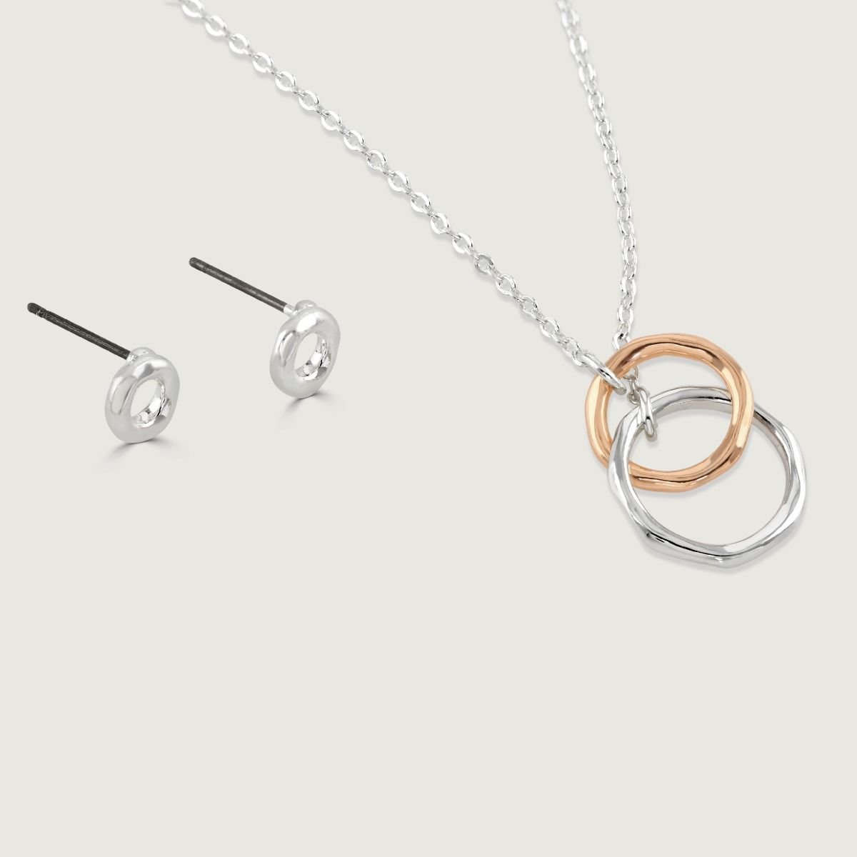 This beautifully delicate pendant features two free flowing rings entwined together and suspended on a silver-plated chain. The rose gold tone and silver-plated rings are complimented with a matching pair of stud earrings.