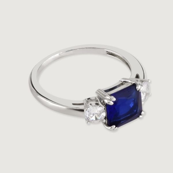 A truly dazzling design, this stunning ring features an emerald cut Sapphire coloured centre stone between two sparkling brilliant cut surrounding stones. 